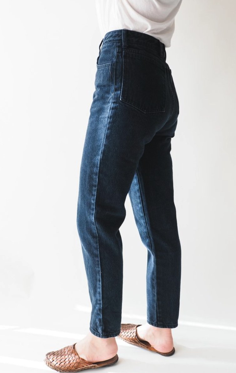 Side view of high-rise dark indigo straight-leg jeans with a clean wash, styled with woven leather mule slides